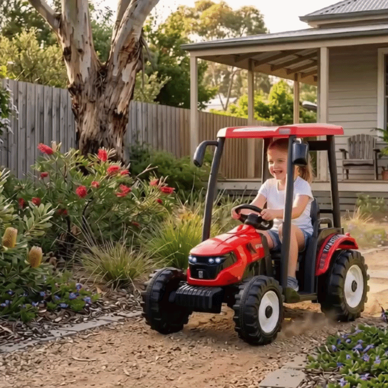 A smiling young girl drives a red toy tractor with a roof on a dirt path through a lush backyard garden.