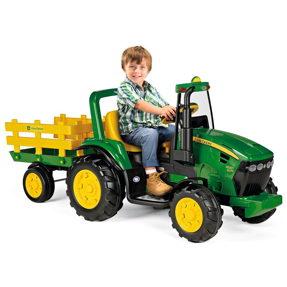 Child sitting on a green toy tractor with a yellow trailer on a white background