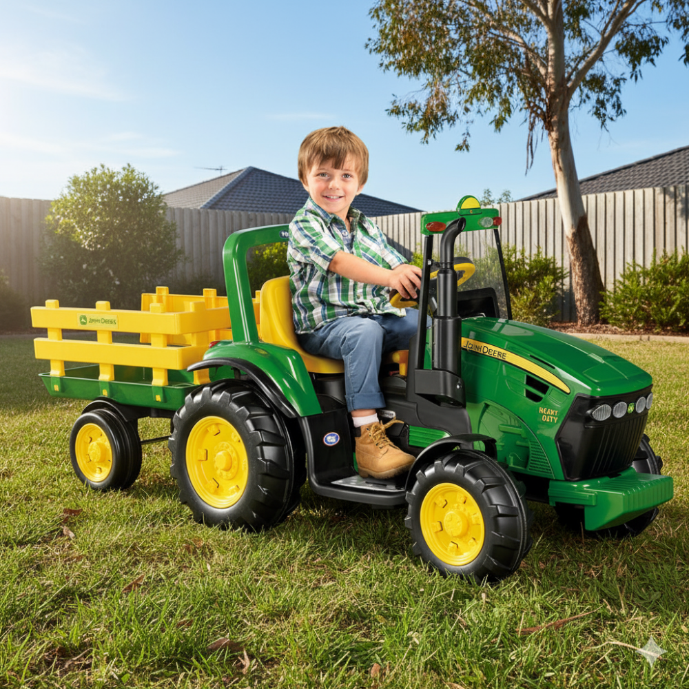 Child playing with a green toy tractor and yellow trailer in a backyard.