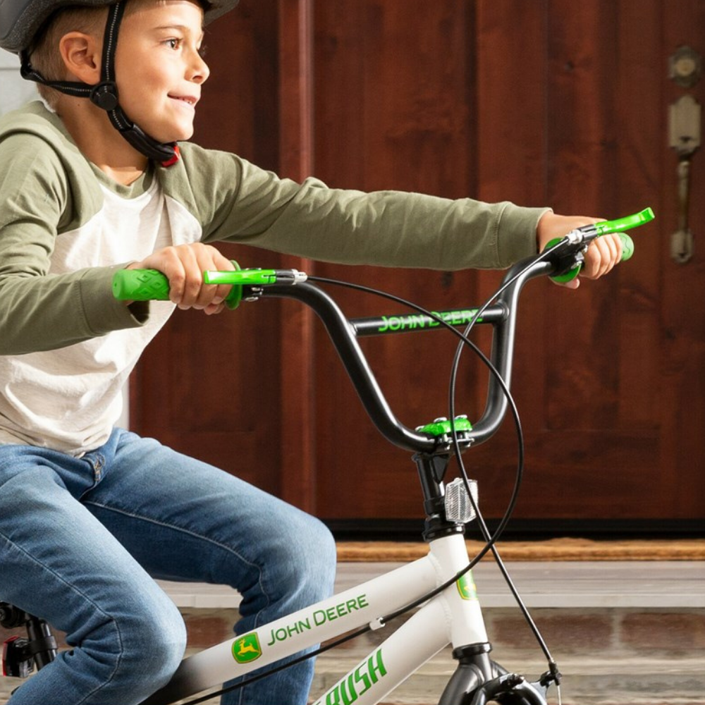 Child sitting on a John Deere bicycle indoors