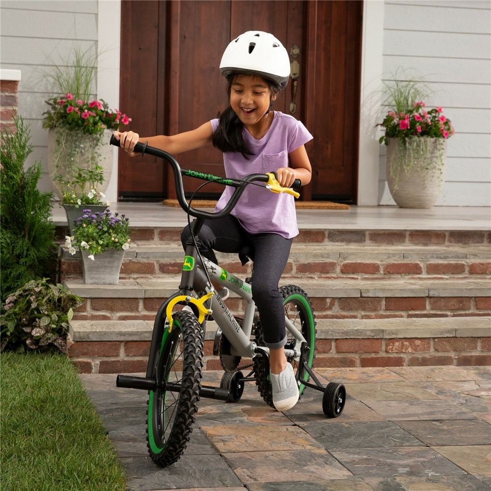 Child riding a bicycle with training wheels on a sidewalk in front of a house.