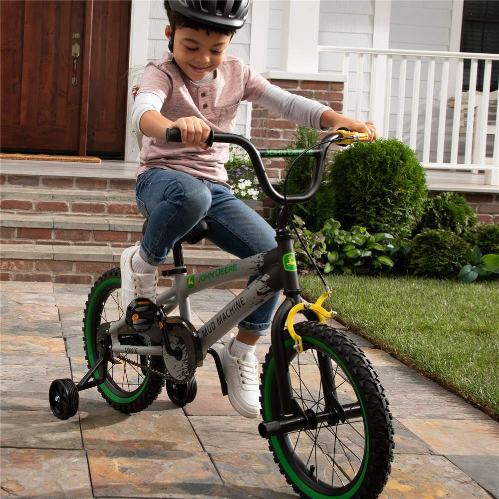 Child riding a bicycle with training wheels on a driveway.