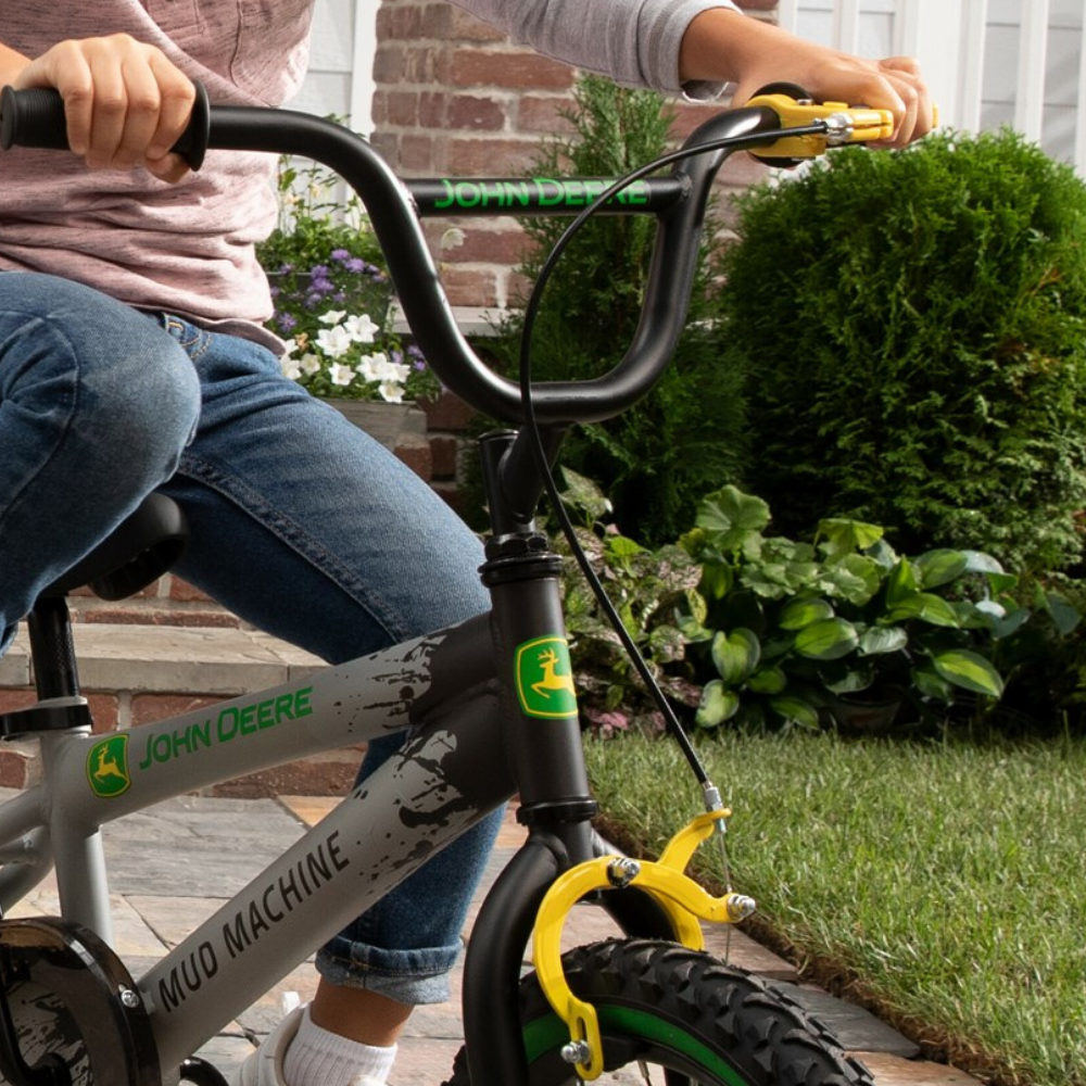 Child riding a John Deere bike in a garden setting