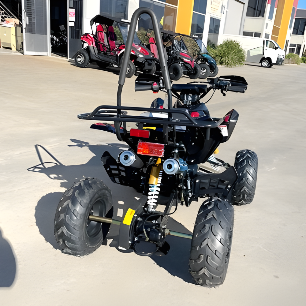 Black ATV parked on a concrete surface with buildings and other vehicles in the background.