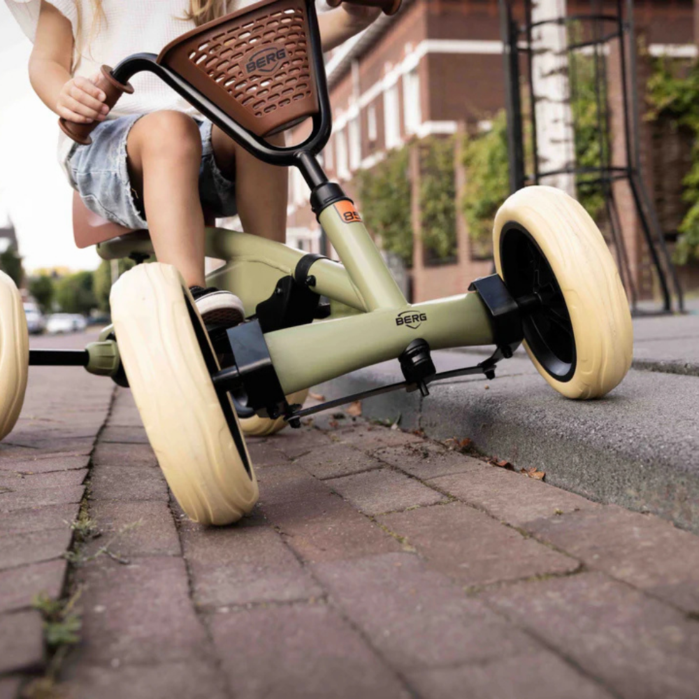 Child riding a green and beige Berg scooter on a paved path.