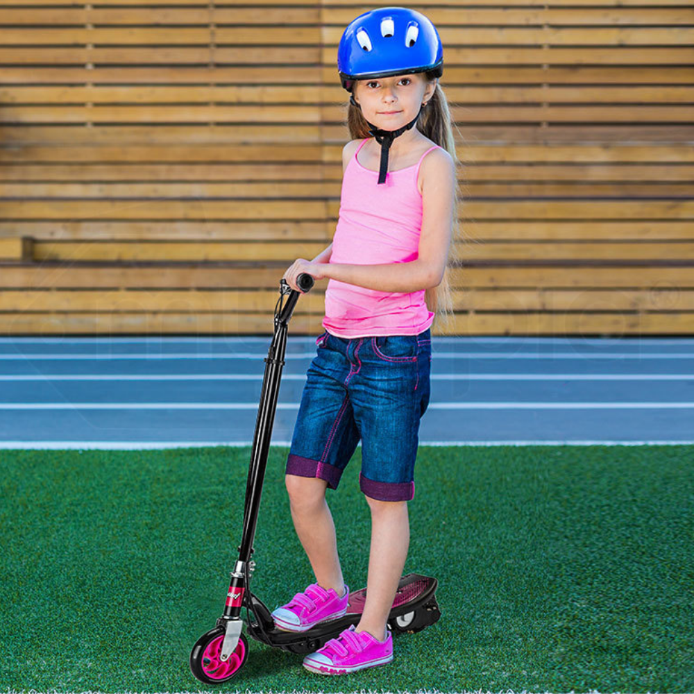 Young girl with a scooter and helmet on a grassy area with wooden steps in the background