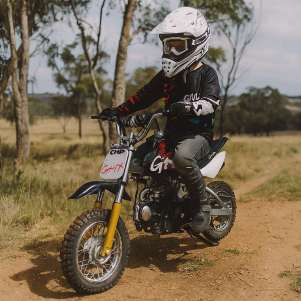 Outdoor action shot of a child riding the GMX dirt bike on a dusty trail, wearing full safety gear.