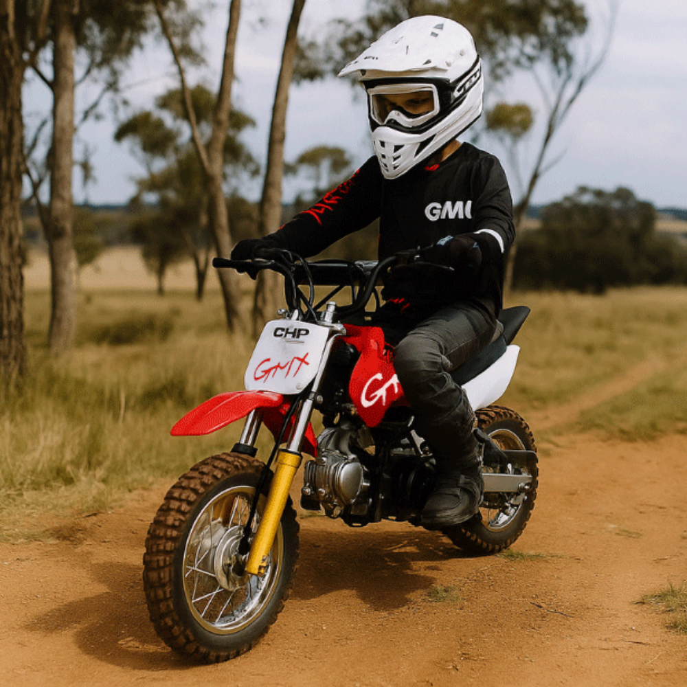 Action shot of a child riding the red GMX dirt bike on a dirt path, wearing a white helmet and black riding gear.