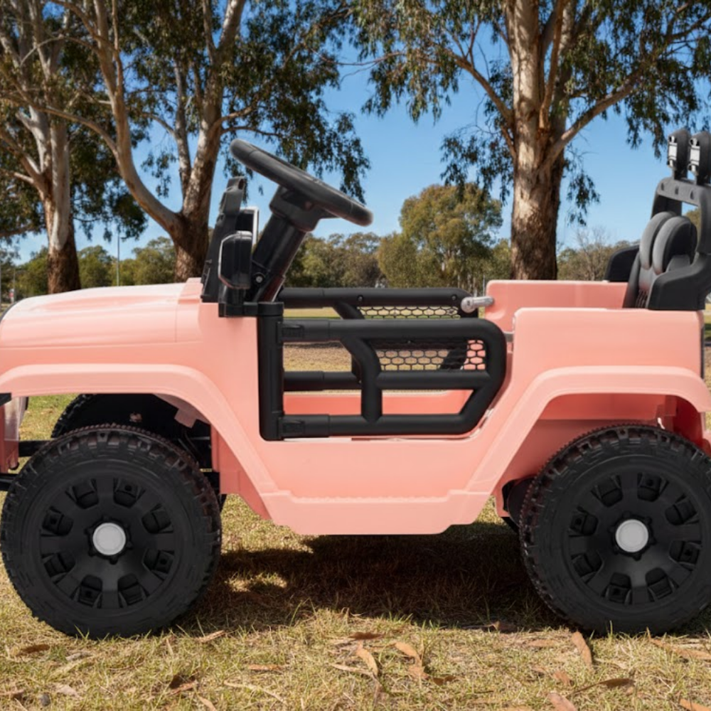 Pink toy jeep with black wheels on a grassy area with trees in the background