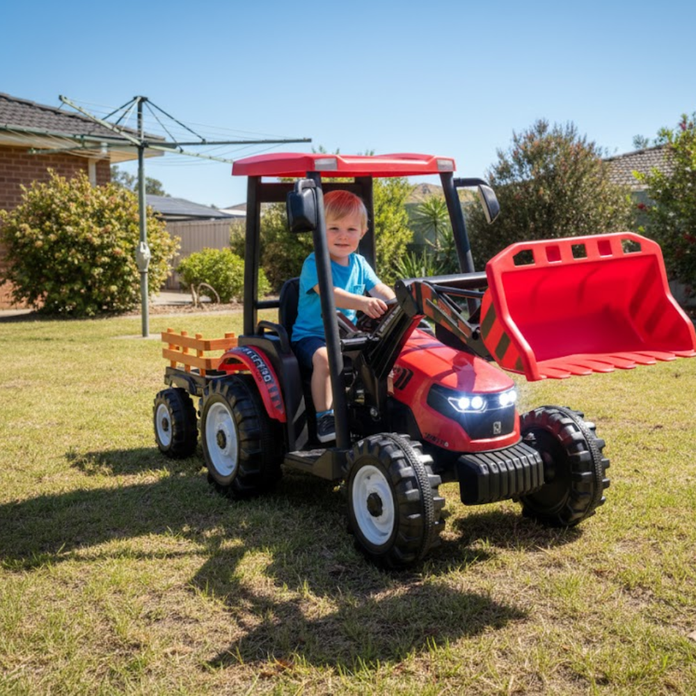 Child sitting in a red toy tractor with a front loader on a grassy area.