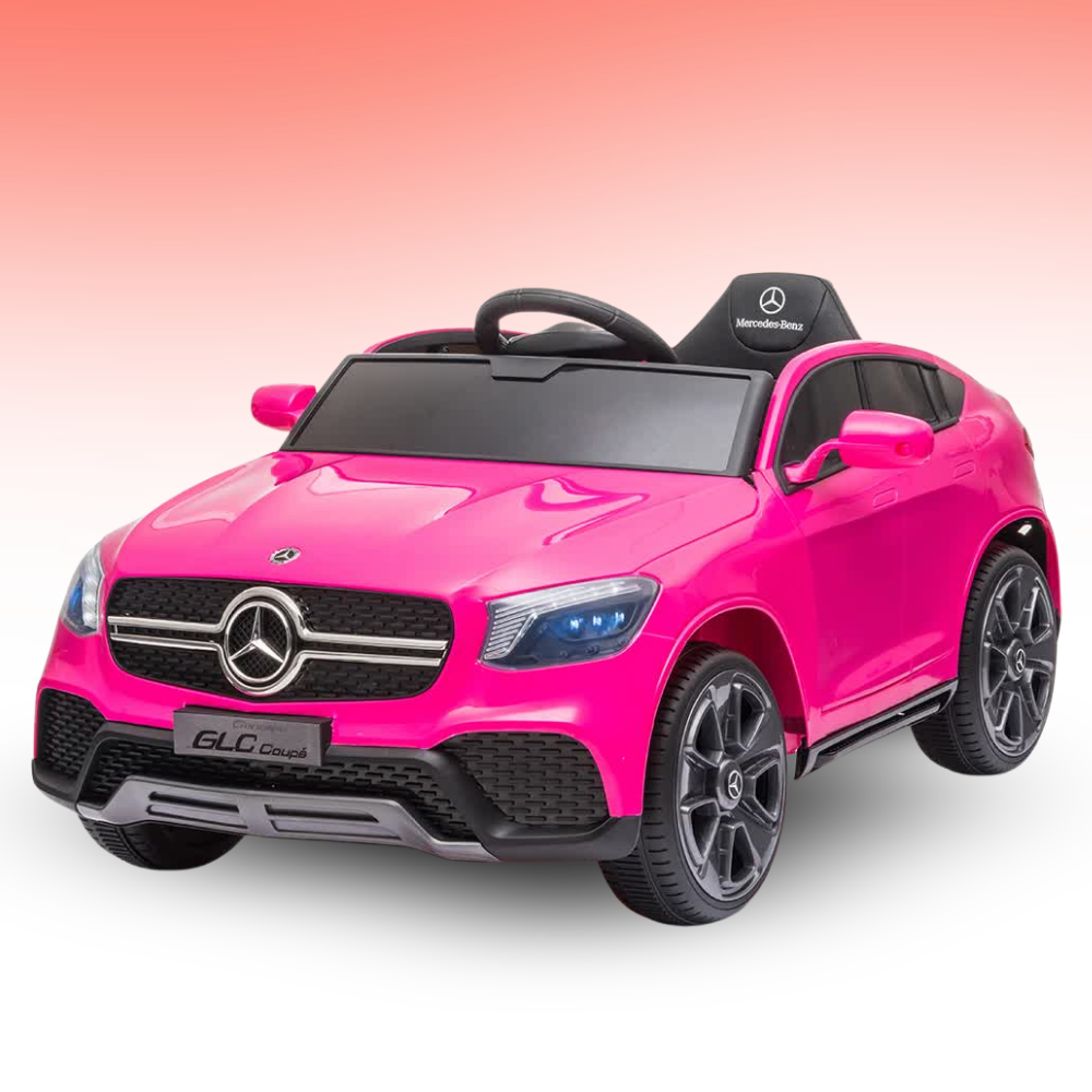 A bright pink Mercedes-Benz GLC Coupe kids' ride-on toy car with black wheels, a black steering wheel, and a black seat, shown on a white background with a pink gradient sky.