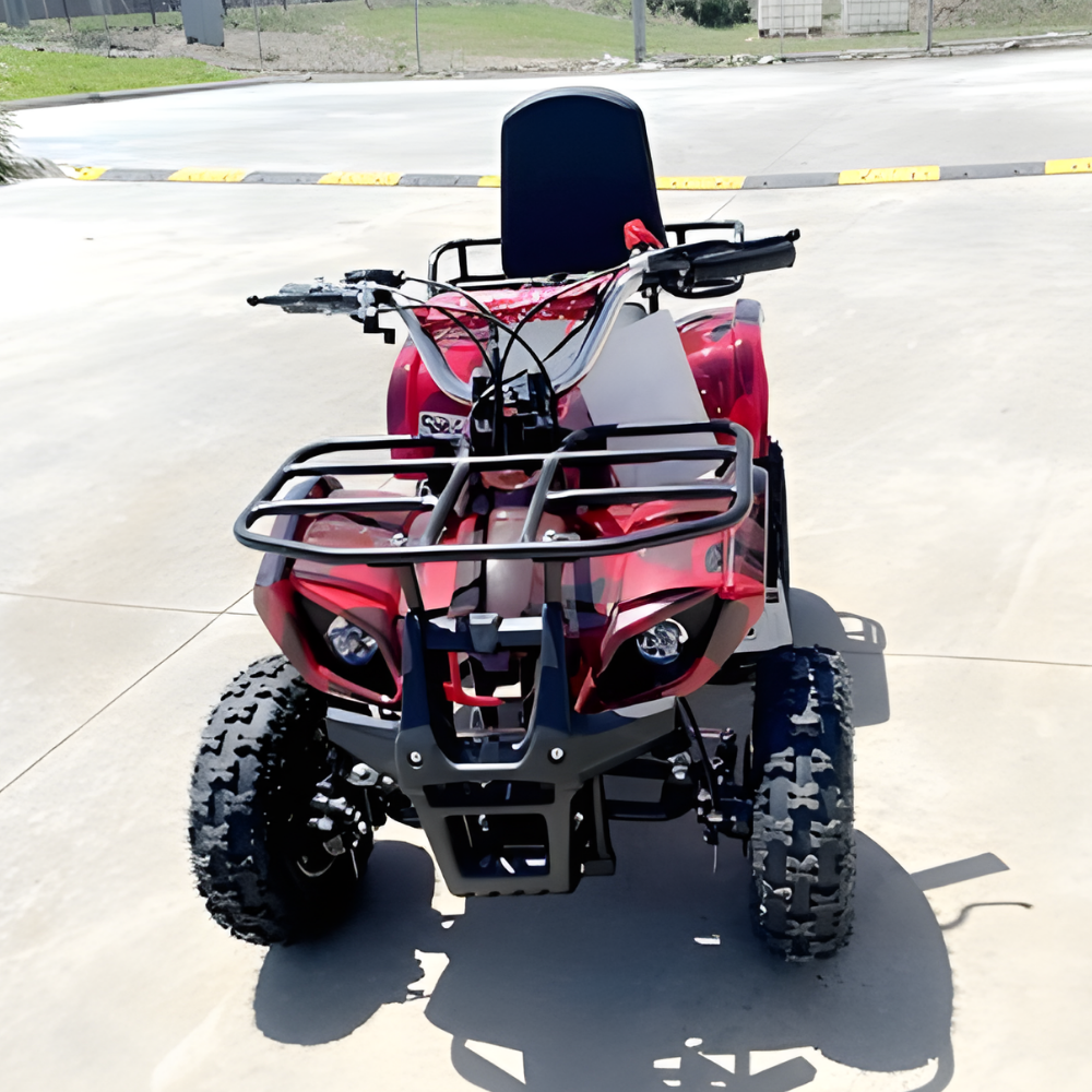 Red and black ATV parked on a paved surface with grass and a fence in the background.