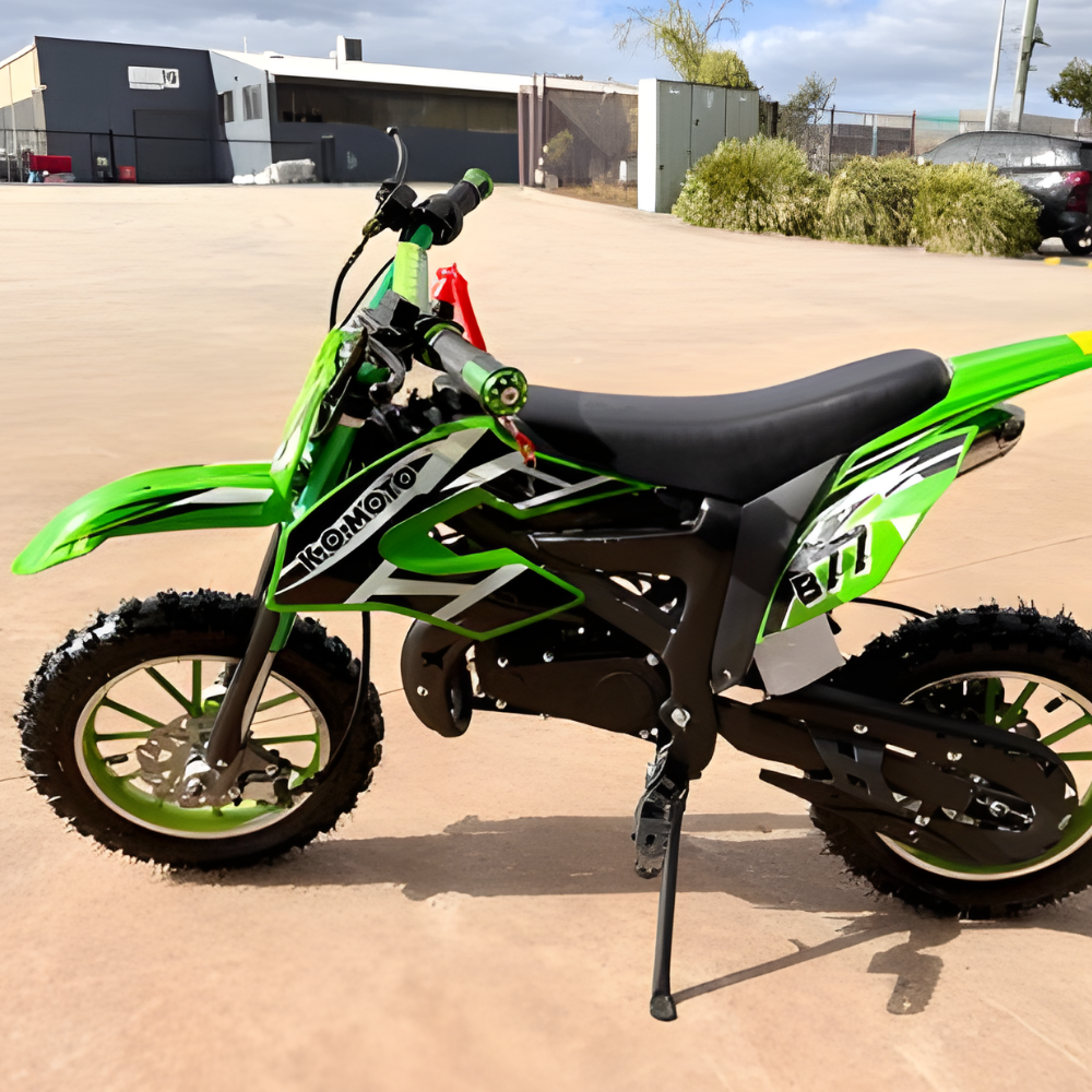 Green and black dirt bike on a concrete surface with buildings and cars in the background