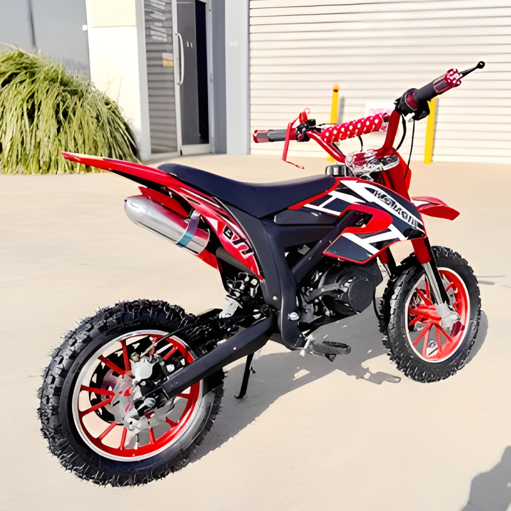 Red and black dirt bike parked on a concrete surface with a building in the background.