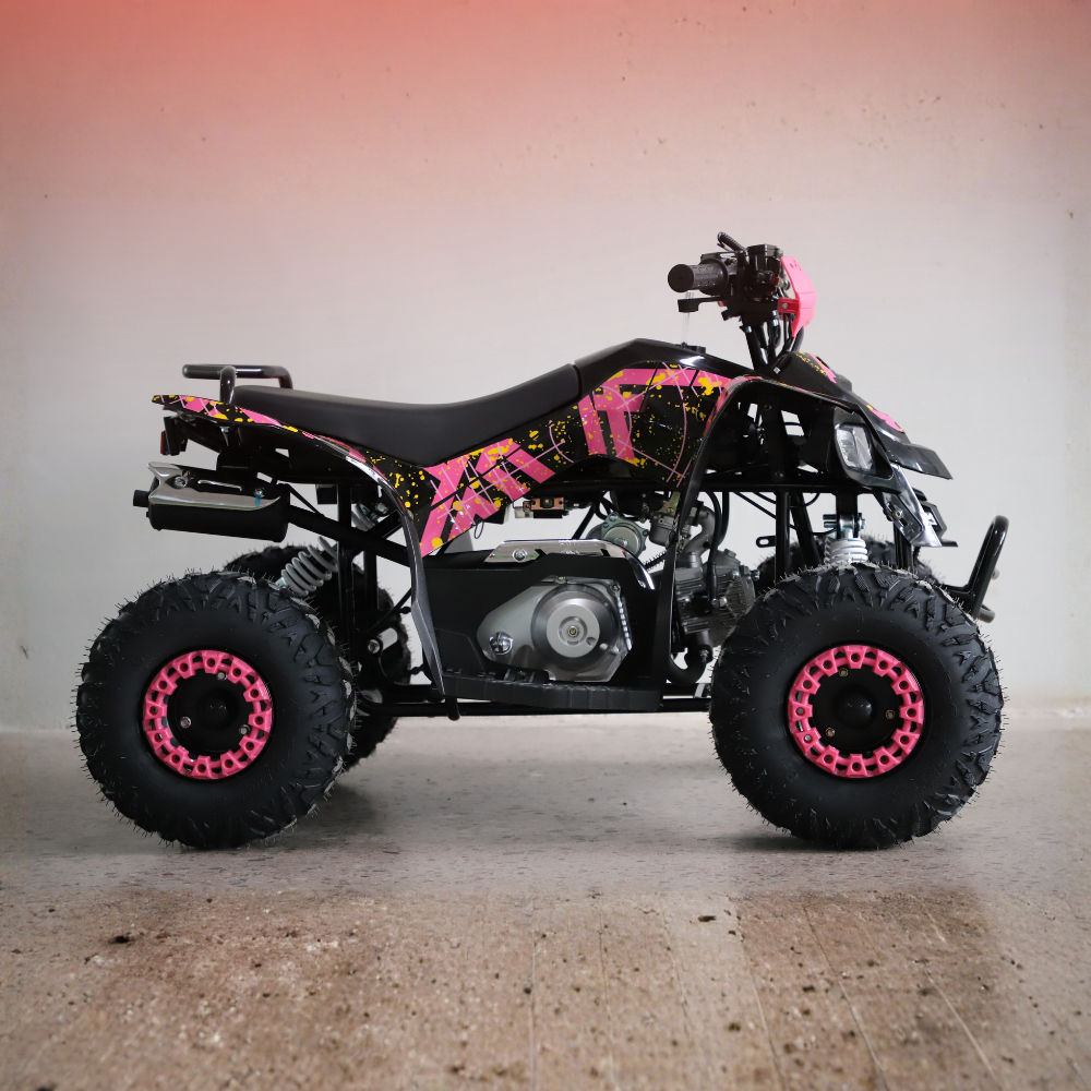 A small black ATV with bright pink and yellow graphic decals, featuring large knobby tires with pink rims, photographed against a plain indoor wall with a warm gradient.