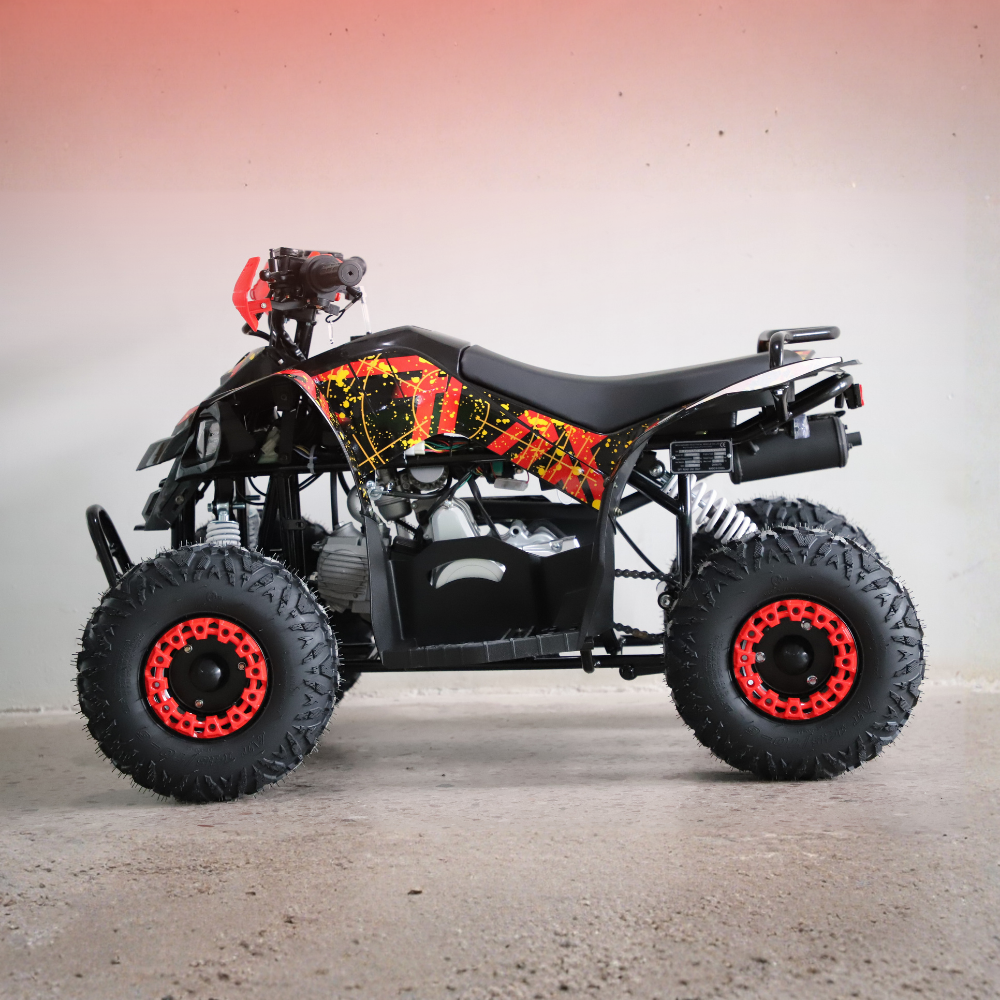 A black quad bike ATV with a vibrant orange, yellow, and red graphic wrap on the side panels, featuring large knobby off-road tires with red rims, photographed in profile against a plain studio backdrop.