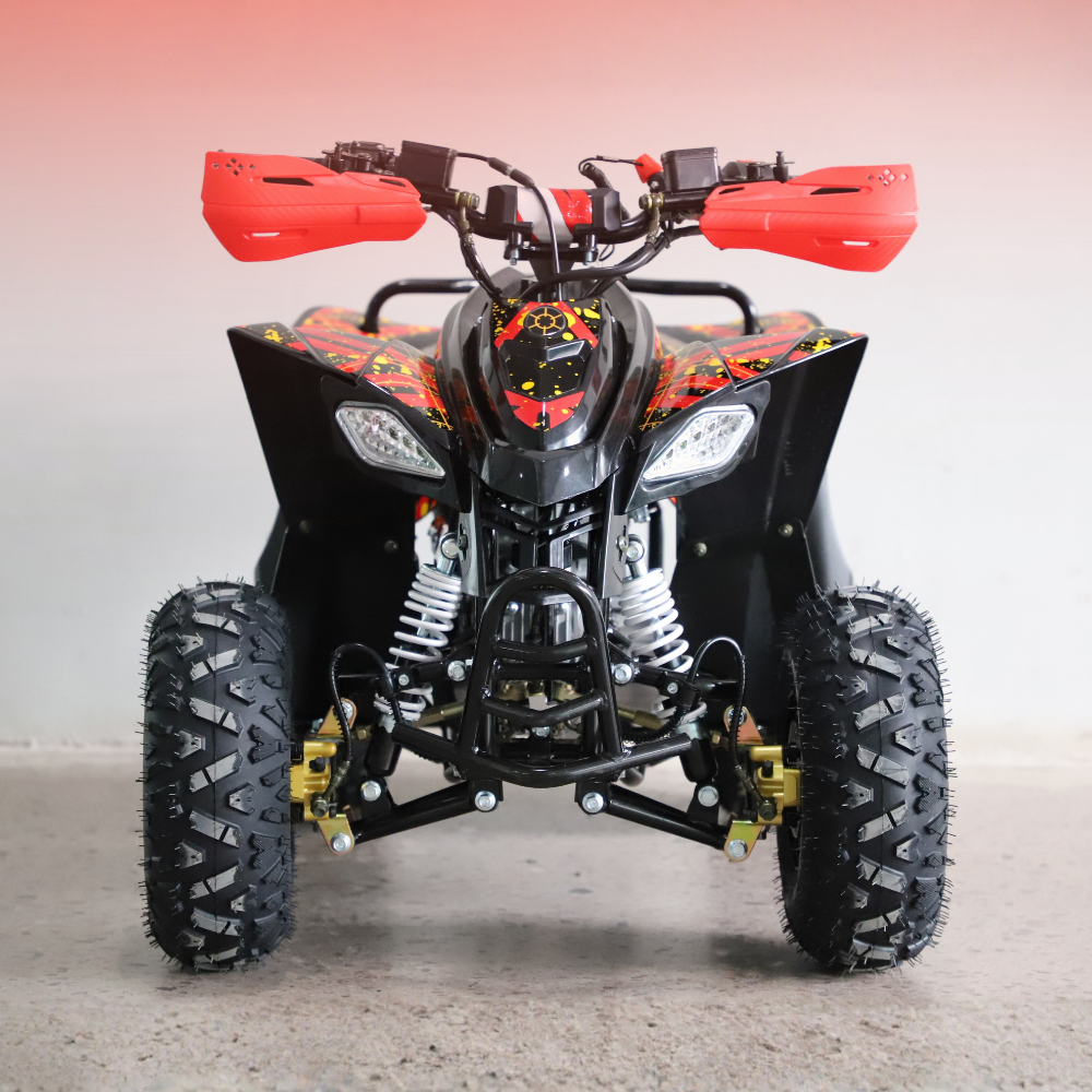 A black and red ATV with large knobby tires, red handlebar grips, and a front protective bumper, photographed against a plain light gray wall.