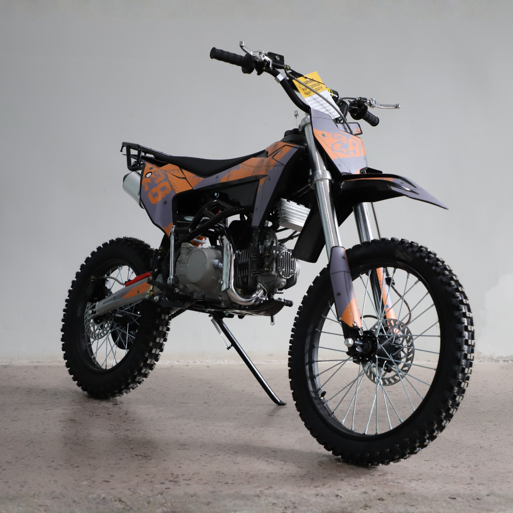 A small off-road dirt bike with a black and orange color scheme, standing on its kickstand in a studio setting with a light gray background.