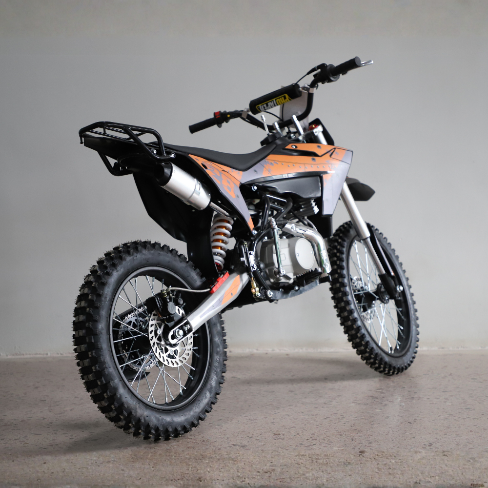 An off-road dirt bike with a black and orange color scheme, featuring knobby tires, a rear luggage rack, and a silver exhaust pipe, photographed in a studio setting.