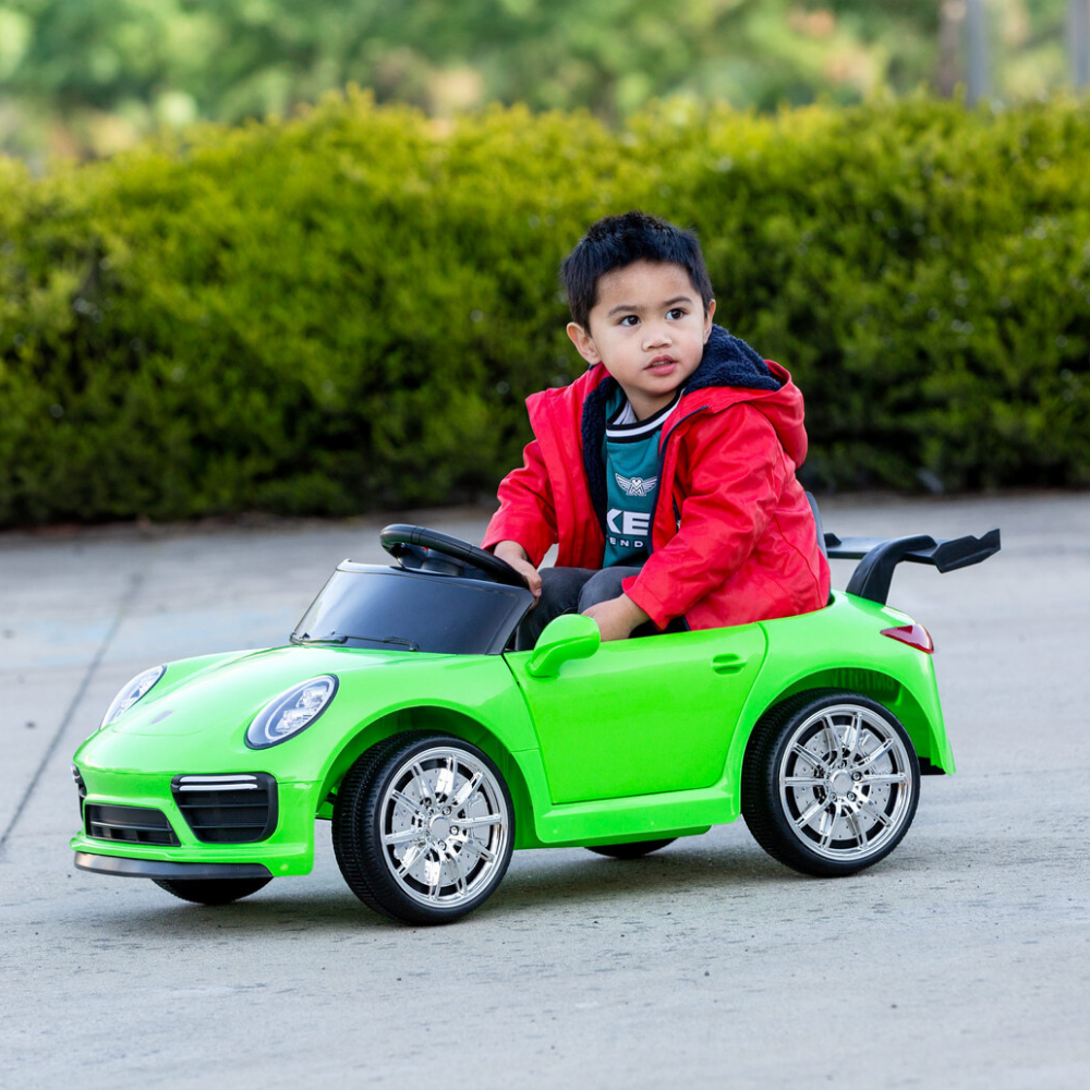 Child in a red jacket sitting in a green toy car outdoors.