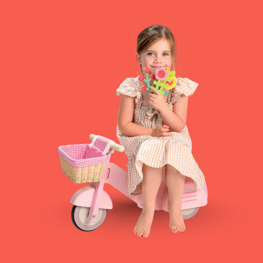 Young girl sitting on a pink tricycle with a basket against a red background