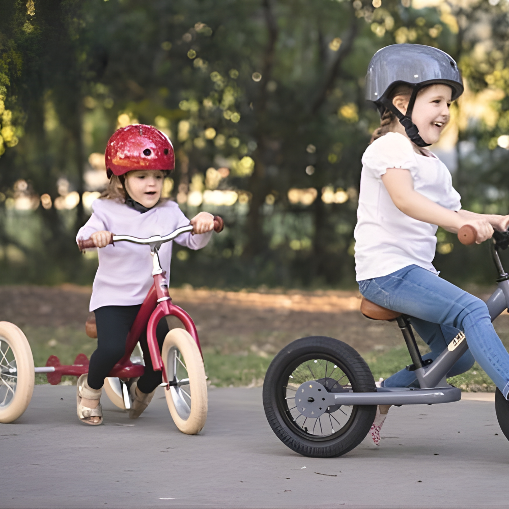 Two children riding balance bikes outdoors with helmets on.