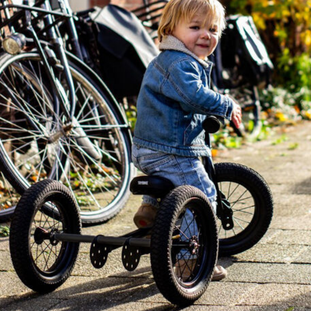 Child riding a tricycle outdoors with bicycles in the background