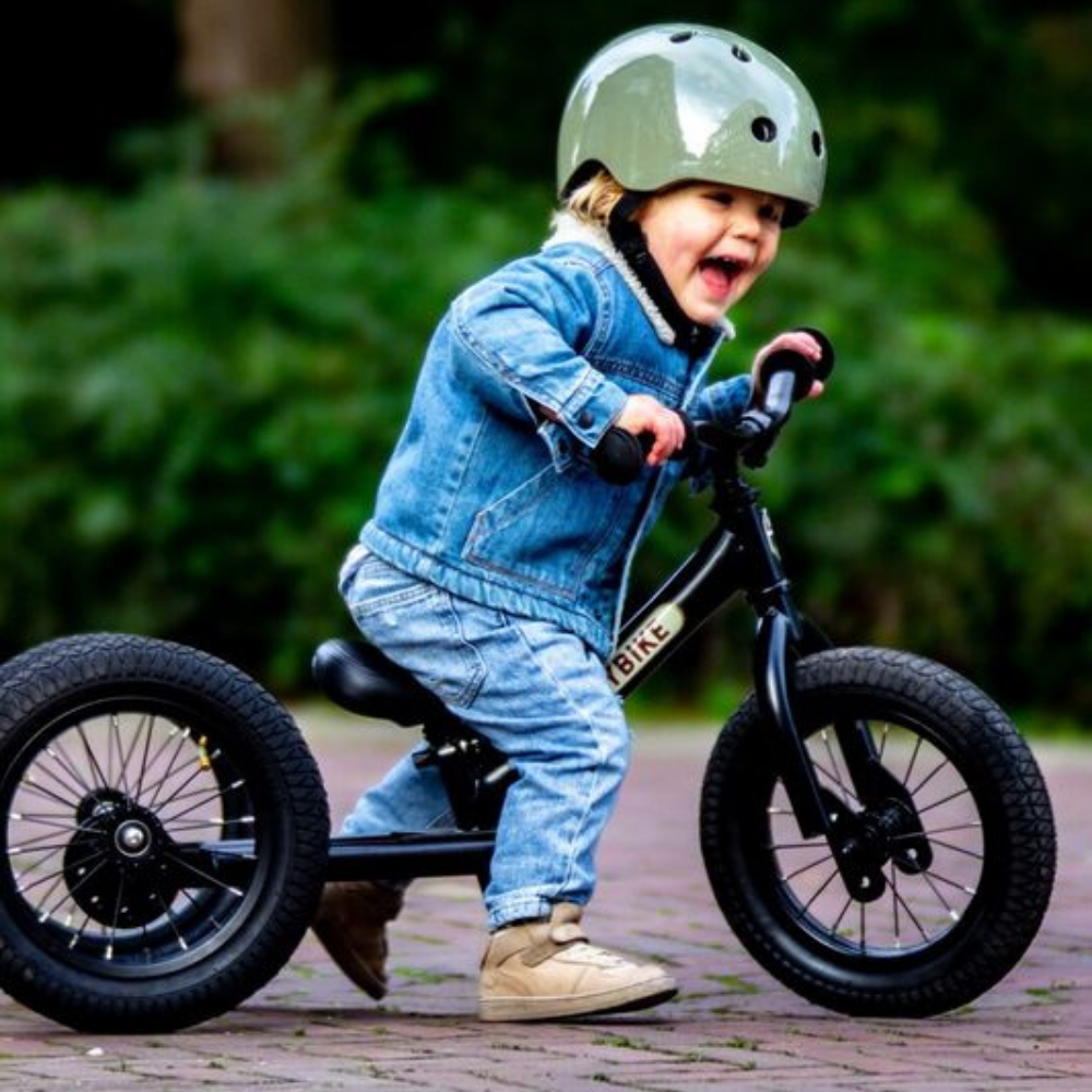 Child riding a balance bike with training wheels outdoors