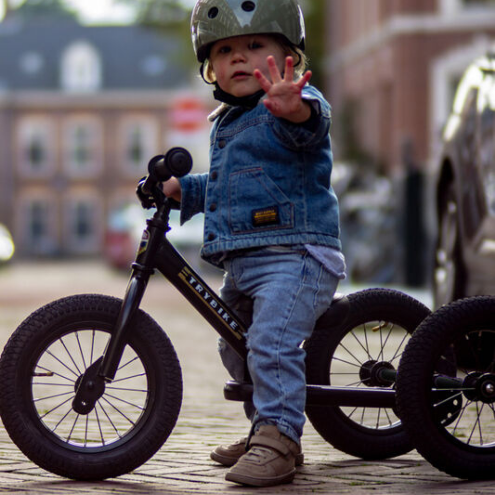 Child on a balance bike with training wheels in an urban setting