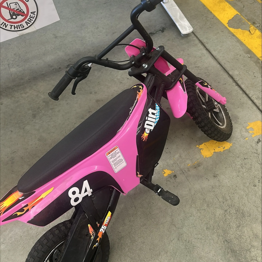 Pink electric kids dirt bike with torn seat and handlebar visible, marked with number 84 and flame decals.