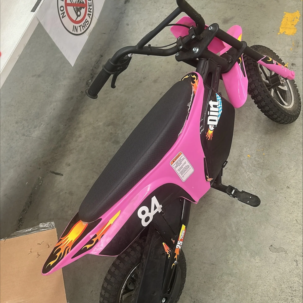Side angle of pink kids dirt bike showing damage to seat edge, black panels, and number 84 on side.