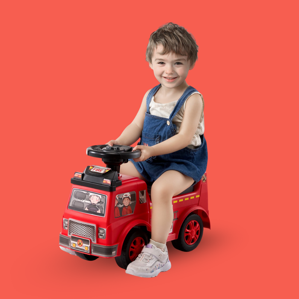 Child sitting on a red toy fire truck against a red background