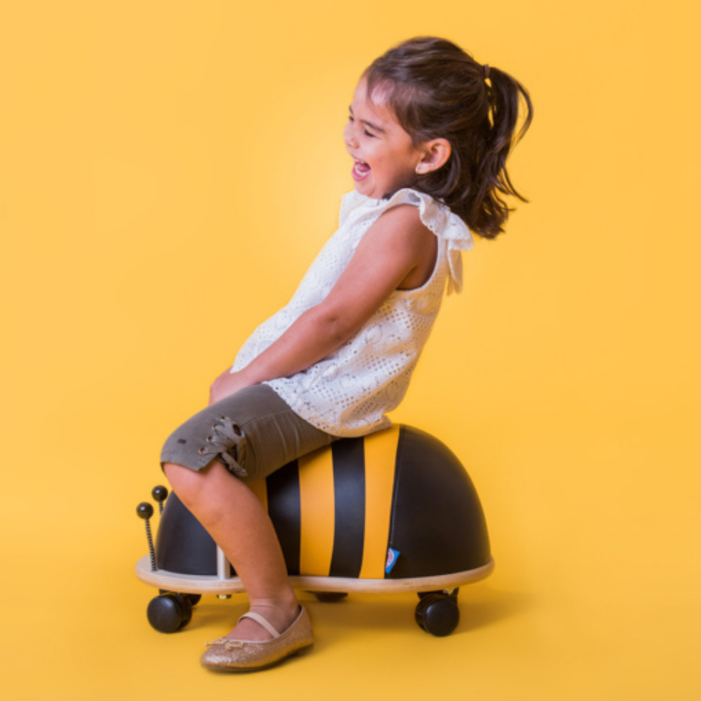 Child sitting on a bee-shaped scooter against a yellow background