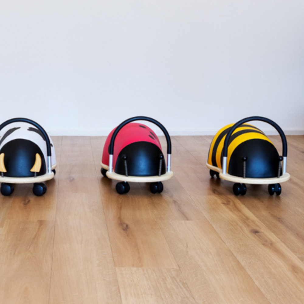Three colorful wheeled toys on a wooden floor with a white background