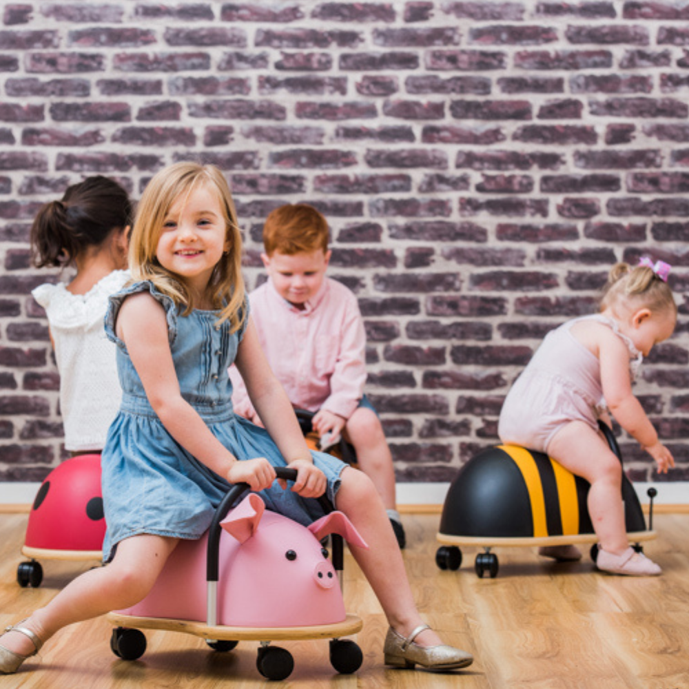 Children playing on colorful balance bikes against a brick wall.