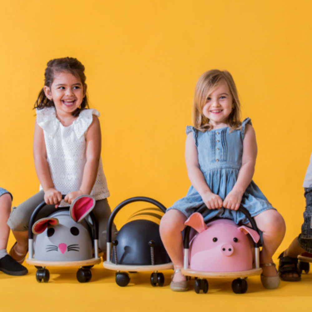 Two children sitting on animal-shaped toy cars against a yellow background