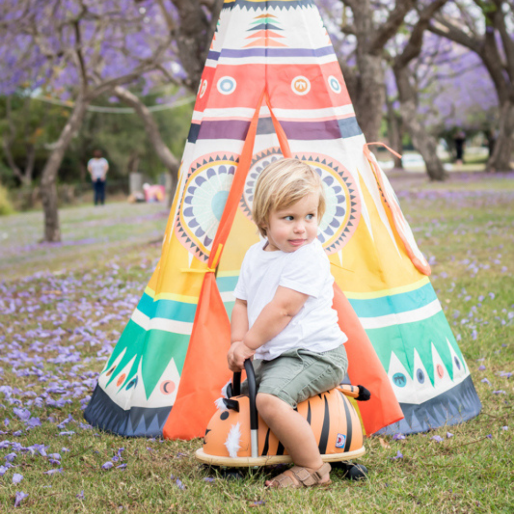 Child playing with a toy car in front of a colorful teepee in a park.