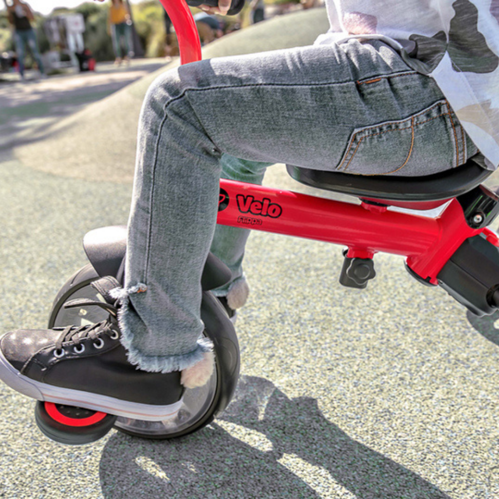 Person riding a red and black Velo scooter on a road.
