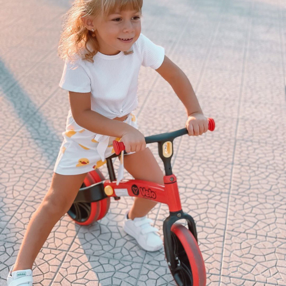 Child riding a red balance bike on a paved surface