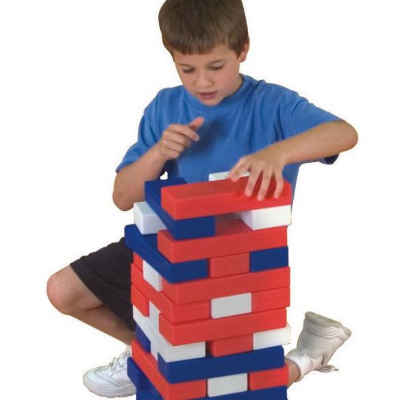 boy in blue shirt playing with timber red, white and blue tumbling blocks