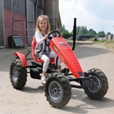 A young girl drives a red Case IH pedal kart on a farm path. It features rugged tractor tires and a vertical exhaust pipe.