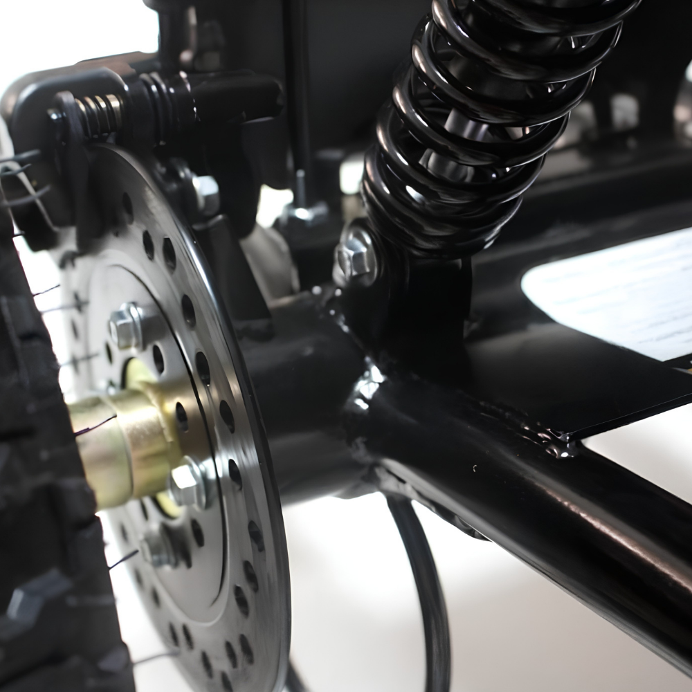 Close-up detail of a black bicycle frame with a rear disc brake, black coil spring, and part of the tire on a light background.