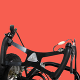 Close-up of a black bicycle frame with handlebars, brake levers, and a small white bulb or connector, shown against a solid red background.