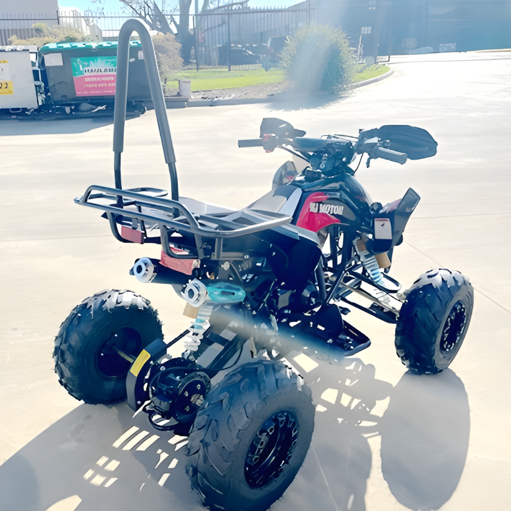 Four-wheeled off-road vehicle on a paved surface with a building and trees in the background.