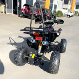Black ATV parked on a concrete surface with buildings and other vehicles in the background.