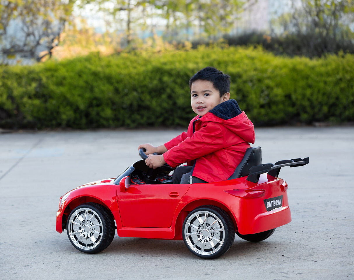 Child enjoying a ride on the red sports toy car in an outdoor setting.