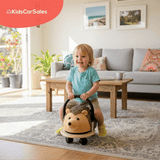 A joyful toddler rides a Wheely Bug Hedgehog ride-on toy in a bright, modern living room with a couch and wooden coffee table.