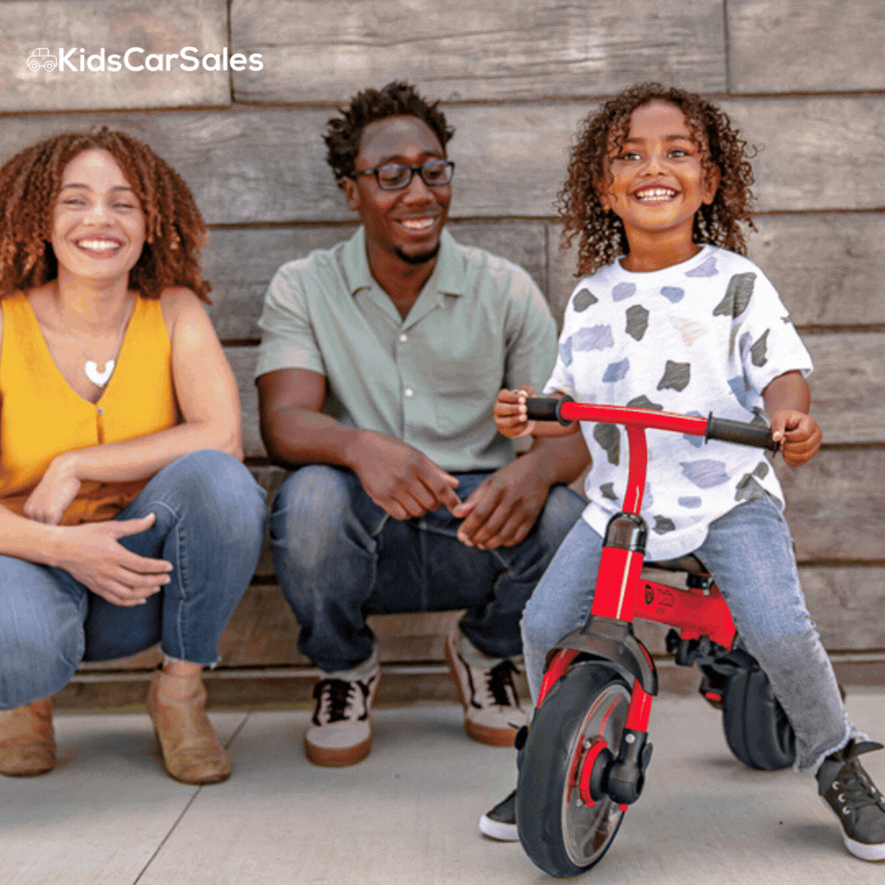 A red and black pedal go-kart with flame decals sits on a dirt road in a sunny, arid outback landscape with trees.