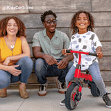 A red and black pedal go-kart with flame decals sits on a dirt road in a sunny, arid outback landscape with trees.