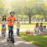 A boy rides an electric scooter past a picnicking family, followed by kids on a bike and scooter.
